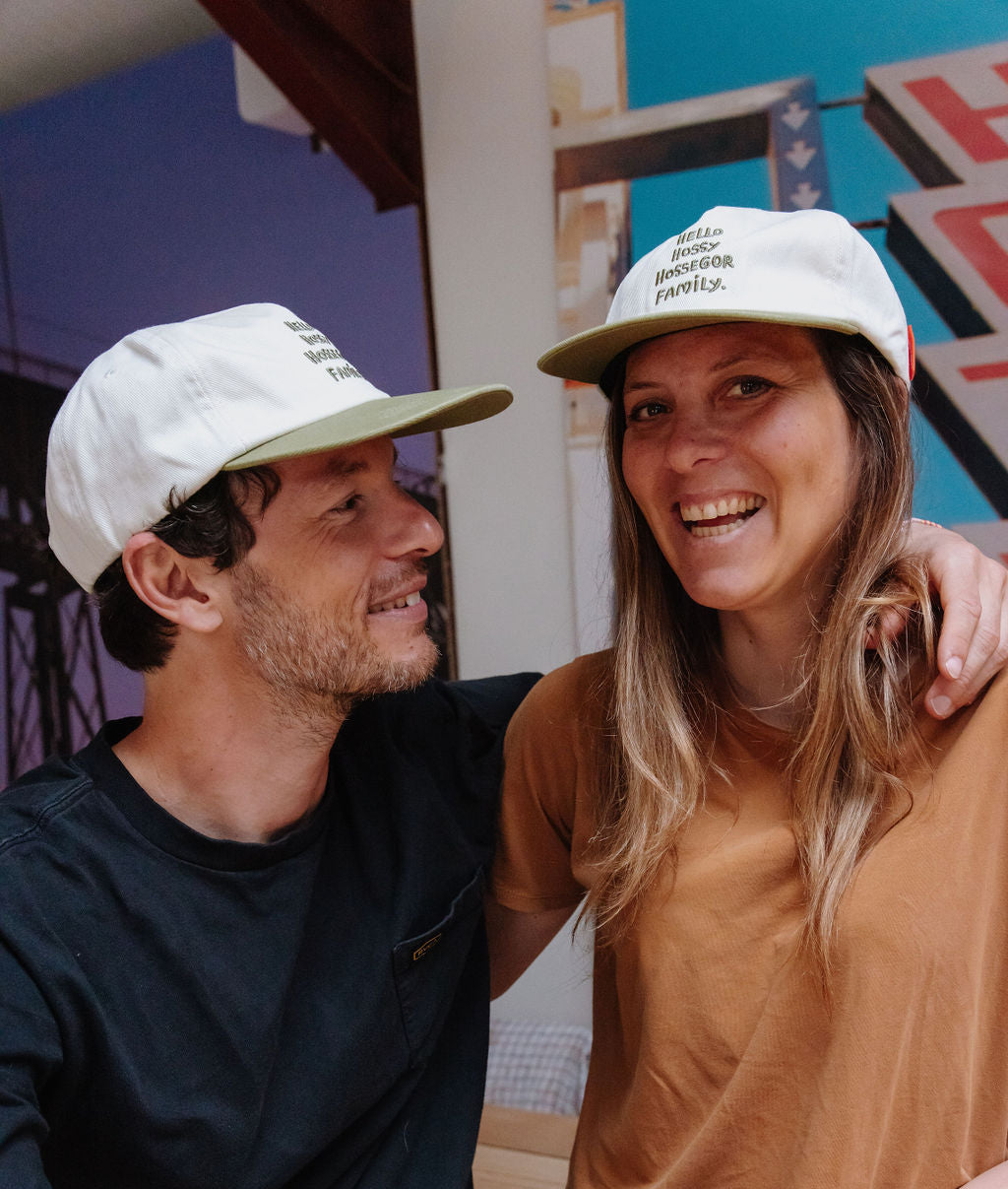 Duo pai e mãe com bonés brancos, palas verdes e bordado com texto Hello Hossy