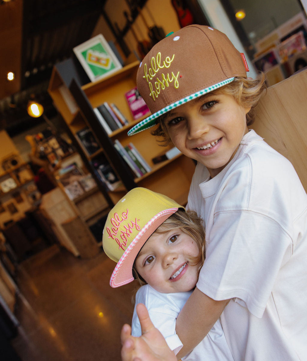 Boné infantil castanho com pala reta e bordado Hello Hossy, e boné amarelo com pala rosa Hello Hossy