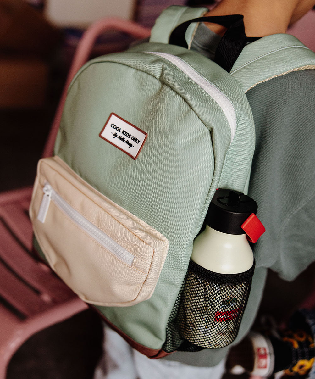 Mochila infantil verde com bolso bege, rede preta, base castanha e patch Hello Hossy
