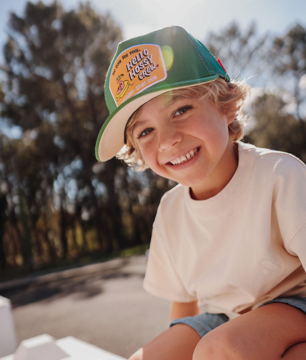 Boné infantil verde com pala curva e patch Hello Hossy, usado por criança Hello Hossy