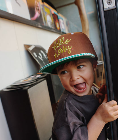 Boné infantil castanho com bordado amarelo, pala reta e padrão xadrez verde Hello Hossy