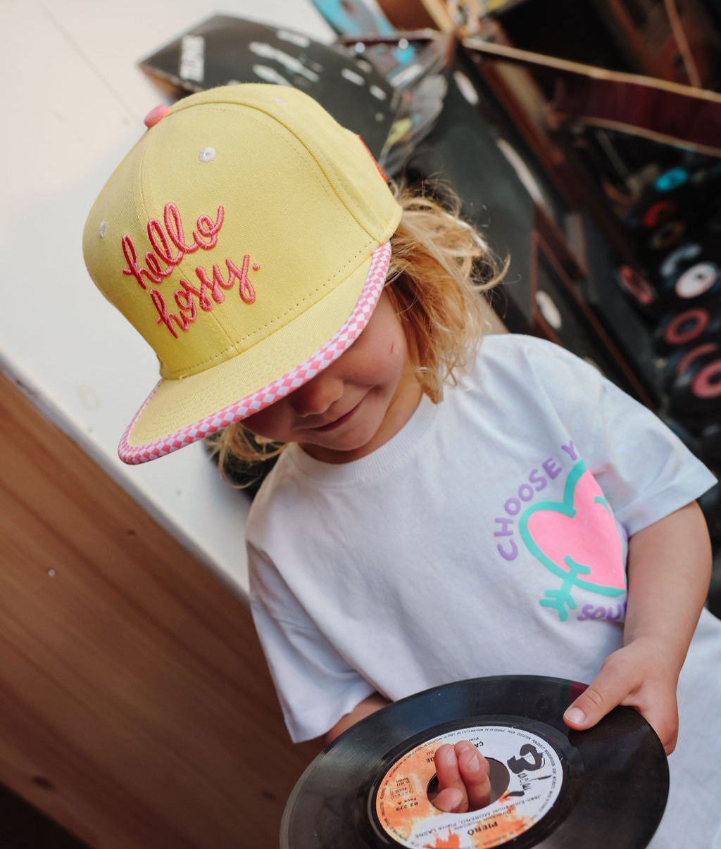 Boné infantil amarelo com bordado rosa, pala reta e padrão xadrez Hello Hossy