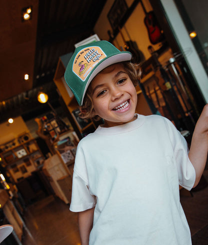 Boné infantil verde com pala curva e patch Hello Hossy, usado por criança Hello Hossy