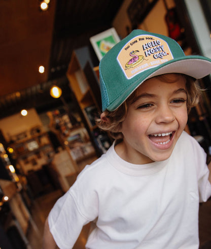 Boné infantil verde com pala curva e patch Hello Hossy, usado por criança Hello Hossy