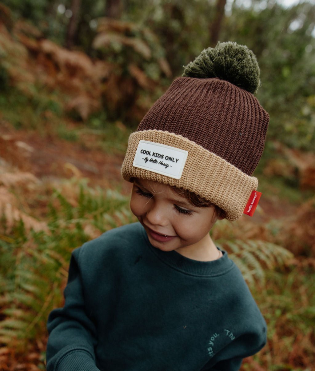 Gorro infantil castanho com rebordo bege, pompom verde e etiqueta cosida Hello Hossy