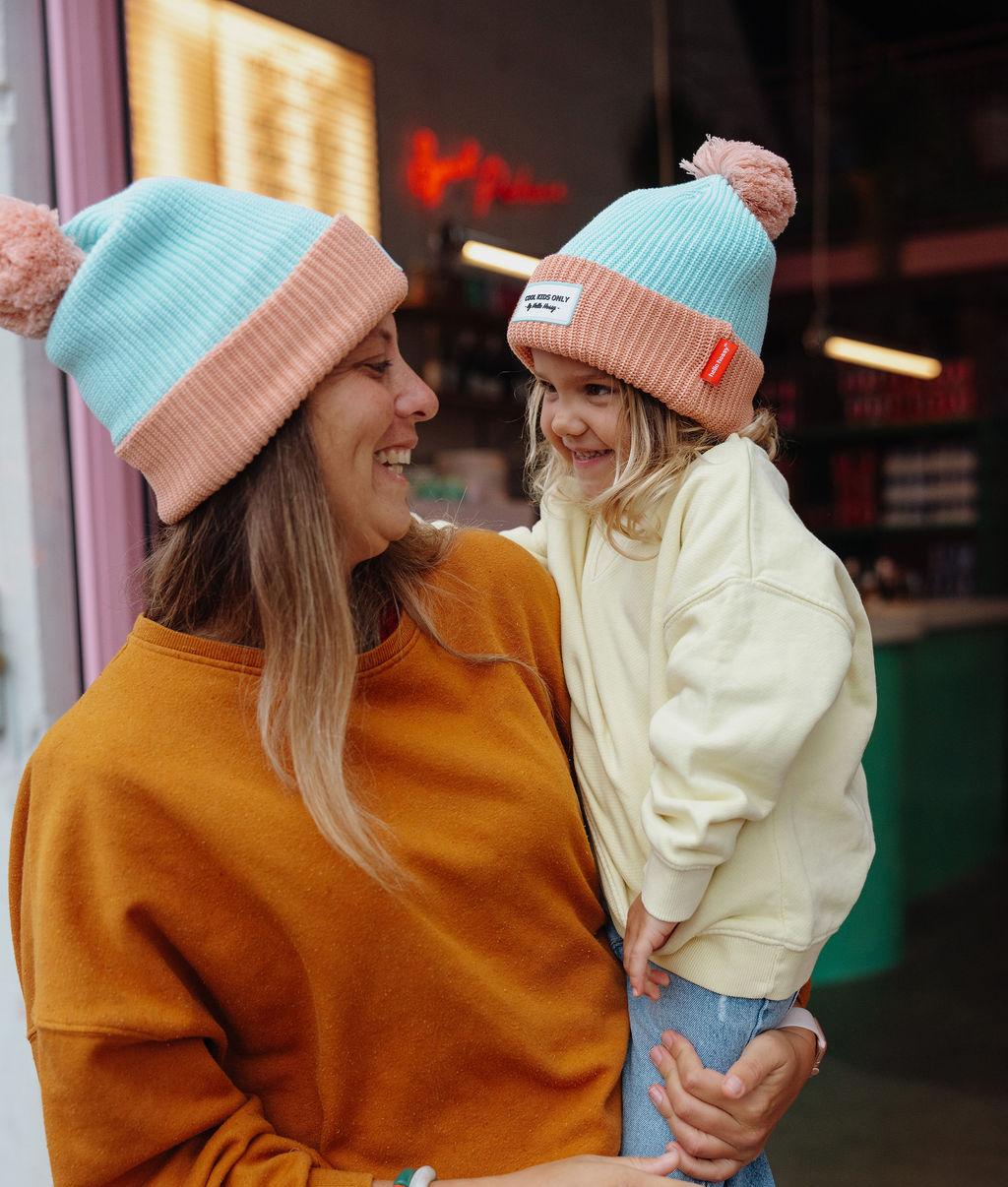 Gorro com pompom Color Block Candy usado por uma mãe com a filha ao colo – foto lifestyle – Hello Hossy