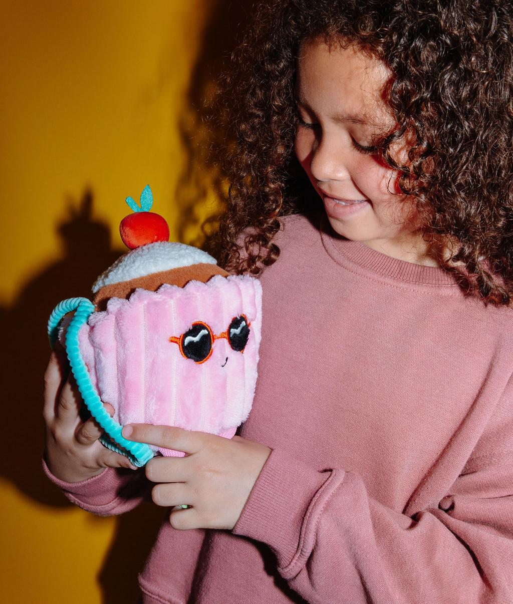 Peluche macia em forma de bolo com uma cereja no topo, Cherry Cake, segurada por uma criança – vista de 3/4 – Hello Hossy