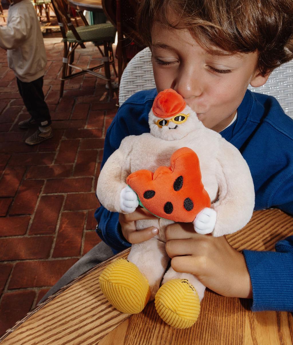 Criança a beijar a Peluche macia em forma de ieti Frosty Yeti pousada numa mesa ao ar livre - foto lifestyle - Hello Hossy