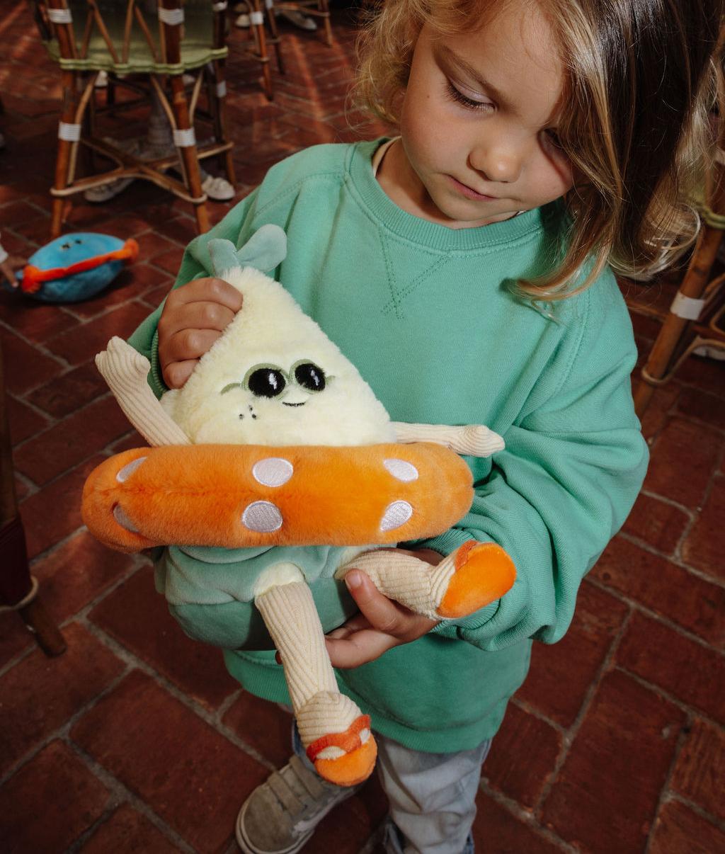 Menina a segurar a Peluche Lemon Splash em forma de limão, com óculos de sol e boia laranja nas mãos - vista de frente - Hello Hossy