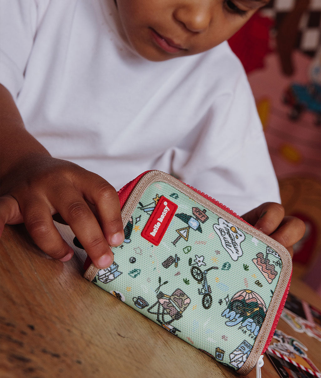 Porta-moedas infantil verde com padrão de viagem e bicicleta, rebordo bege, fecho vermelho Hello Hossy