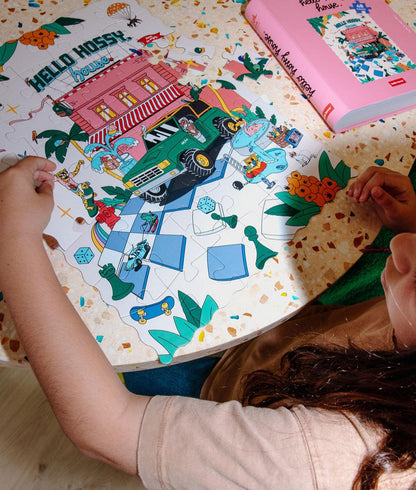 Menina a montar o Puzzle colorido de 48 peças "Hello Hossy House" numa mesa – vista de cima – Hello Hossy