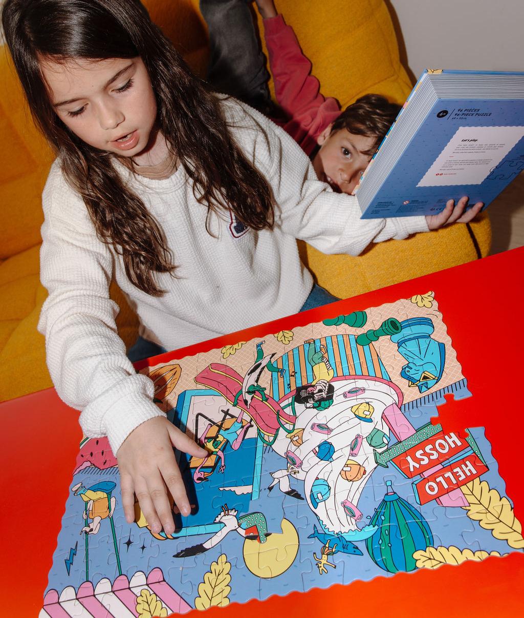 Menina com o Puzzle "Ice Cream Day" montado numa mesa à sua frente, segurando na mão a caixa com efeito de livro – foto lifestyle – Hello Hossy
