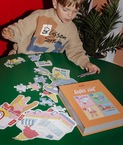 Menino a montar os puzzles coloridos "Just Enjoy" numa mesa, com os modelos à frente – ambiente divertido – Hello Hossy