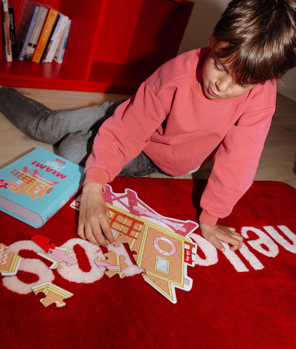 Menino a montar o Puzzle colorido de 28 peças "Miami Plage" num tapete no chão – foto lifestyle – Hello Hossy