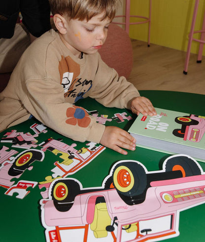Menino com o Puzzle "On The Road" parcialmente montado, a caixa e a ilustração-modelo, sobre uma mesa, à sua frente – foto lifestyle – Hello Hossy
